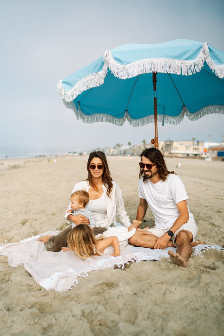 Family relaxing on the beach under a striped umbrella